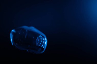 Parlayan, şeffaf mavi bir balon koyu mavi bir arkaplan üzerinde yüzer, yansımalar ve ışık çizgileri fütüristik ve sürrealist bir etki yaratır. Kopyalama alanı içerir.