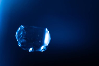 Parlayan, şeffaf mavi bir balon koyu mavi bir arkaplan üzerinde yüzer, yansımalar ve ışık çizgileri fütüristik ve sürrealist bir etki yaratır. Kopyalama alanı içerir.