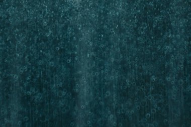 Yumuşak dairesel bokeh ve ince su damlası dokularına sahip koyu bir deniz mavisi soyut arkaplanı karamsar ve atmosferik bir his yaratıyor. Kopyalama alanı içerir.
