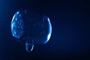 Parlayan, şeffaf mavi bir balon koyu mavi bir arkaplan üzerinde yüzer, yansımalar ve ışık çizgileri fütüristik ve sürrealist bir etki yaratır. Kopyalama alanı içerir.