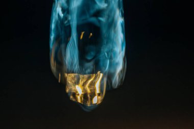 Bozulmuş, yarı saydam sıvı bir şekil, hareketin ortasında asılı, mavi ve altın ışıkla aydınlatılmış, koyu bir arkaplanda çizgiler çiziyor. Kopyalama alanı içerir.