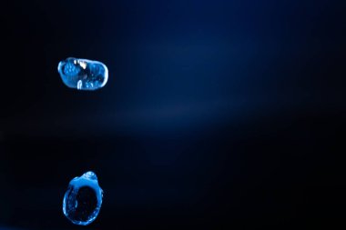 İki şeffaf mavi sıvı damlacık karanlık, minimum bir ortamda asılı, yansımalarla yavaşça parlayan ve geleceksel, ruhani bir hava yaratıyor. Kopyalama alanı içerir.