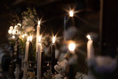 Sıcak, romantik bir atmosfer, arka planda hafifçe bulanık beyaz çiçeklerle çevrili süslü tutucularda parlayan mumlarla oluşur. Kopyalama alanı içerir.