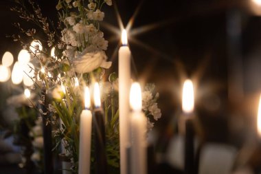 Sıcak, romantik bir atmosfer, arka planda hafifçe bulanık beyaz çiçeklerle çevrili süslü tutucularda parlayan mumlarla oluşur. Kopyalama alanı içerir.