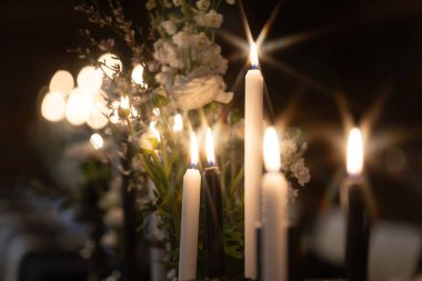 Sıcak, romantik bir atmosfer, arka planda hafifçe bulanık beyaz çiçeklerle çevrili süslü tutucularda parlayan mumlarla oluşur. Kopyalama alanı içerir.