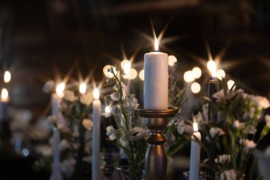 Sıcak, romantik bir atmosfer, arka planda hafifçe bulanık beyaz çiçeklerle çevrili süslü tutucularda parlayan mumlarla oluşur. Kopyalama alanı içerir.