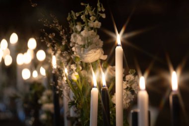 Sıcak, romantik bir atmosfer, arka planda hafifçe bulanık beyaz çiçeklerle çevrili süslü tutucularda parlayan mumlarla oluşur. Kopyalama alanı içerir.