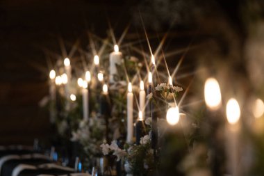 Sıcak, romantik bir atmosfer, arka planda hafifçe bulanık beyaz çiçeklerle çevrili süslü tutucularda parlayan mumlarla oluşur. Kopyalama alanı içerir.