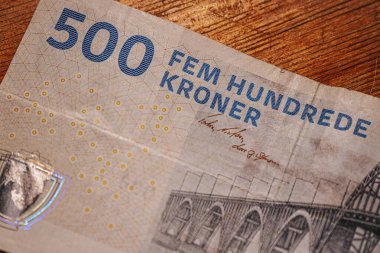 Tahta bir yüzeye yerleştirilmiş köprü çizimleri ve güvenlik unsurlarının yer aldığı Danimarka 'dan gelen 500 DKK banknotunun ayrıntılı bir görüntüsü.