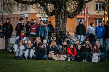 Bir grup insan büyük bir LED ekranda spor maçı izlemek için dışarıda toplandı. Kırmızı elbiseli taraftarlar tezahürat yapıyordu. Hokey hayranları canlı yayın izliyor. 10.05.2025 Valmiera, Letonya