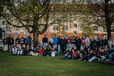 Bir grup insan büyük bir LED ekranda spor maçı izlemek için dışarıda toplandı. Kırmızı elbiseli taraftarlar tezahürat yapıyordu. Hokey hayranları canlı yayın izliyor. 10.05.2025 Valmiera, Letonya