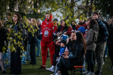 Bir grup insan büyük bir LED ekranda spor maçı izlemek için dışarıda toplandı. Kırmızı elbiseli taraftarlar tezahürat yapıyordu. Hokey hayranları canlı yayın izliyor. 10.05.2025 Valmiera, Letonya