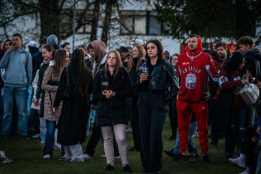 Bir grup insan büyük bir LED ekranda spor maçı izlemek için dışarıda toplandı. Kırmızı elbiseli taraftarlar tezahürat yapıyordu. Hokey hayranları canlı yayın izliyor. 10.05.2025 Valmiera, Letonya