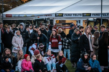 Çoğu battaniye ve sırt çantalarıyla çimlerin üzerinde oturan bir grup insan, serin havada bir açık hava etkinliğini dikkatle izliyor. 10.05.2025 Valmiera, Letonya