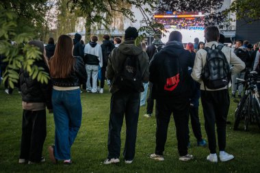 Bir grup insan büyük bir LED ekranda spor maçı izlemek için dışarıda toplandı. Kırmızı elbiseli taraftarlar tezahürat yapıyordu. Hokey hayranları canlı yayın izliyor. 10.05.2025 Valmiera, Letonya