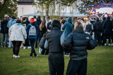 Bir grup insan büyük bir LED ekranda spor maçı izlemek için dışarıda toplandı. Kırmızı elbiseli taraftarlar tezahürat yapıyordu. Hokey hayranları canlı yayın izliyor. 10.05.2025 Valmiera, Letonya