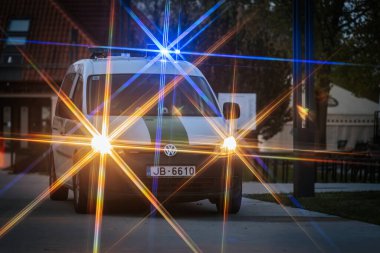 Mavi ve sarı ışıklı bir polis minibüsü, dramatik bir vurgu için yıldız patlaması etkisi yaratarak alacakaranlıkta olay yerini aydınlatıyor. 10.05.2025 Valmiera, Letonya