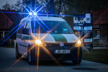Mavi ve sarı ışıklı bir polis minibüsü, dramatik bir vurgu için yıldız patlaması etkisi yaratarak alacakaranlıkta olay yerini aydınlatıyor. 10.05.2025 Valmiera, Letonya