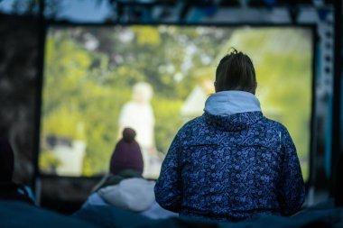 Sıcak ceketli ve şapkalı insanlar, Kino Pedlis festivali sırasında açık ekrana yansıtılan ve rahat armut çuvalları ve bayrak ile çevrili bir film izliyorlar. 10.05.2025 Valmiera, Letonya
