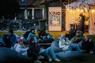 Sıcak ceketli ve şapkalı insanlar, Kino Pedlis festivali sırasında açık ekrana yansıtılan ve rahat armut çuvalları ve bayrak ile çevrili bir film izliyorlar. 10.05.2025 Valmiera, Letonya