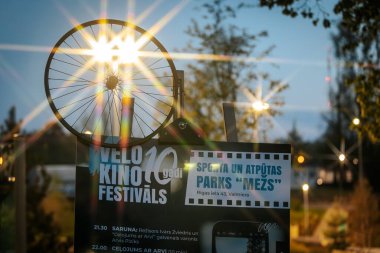 Letonya 'nın Valmiera kentindeki Velo Kino Festivalleri için bir arka ışıklandırma tabelası. Bisiklet tekeri ve parlak sokak lambaları alacakaranlıkta yıldız patlaması etkisi yaratıyor. 10.05.2025 Valmiera, Letonya