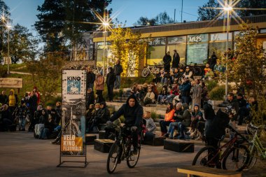 İnsanlar Kino Pedalis festivali sırasında ön planda tanıtım pankartıyla merdivenlerde oturup açık hava film gösterimi izliyor. 10.05.2025 Valmiera, Letonya
