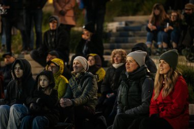 İnsanlar Kino Pedalis festivali sırasında ön planda tanıtım pankartıyla merdivenlerde oturup açık hava film gösterimi izliyor. 10.05.2025 Valmiera, Letonya