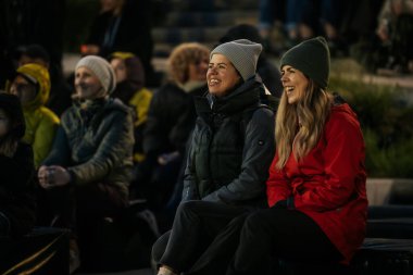 İnsanlar Kino Pedalis festivali sırasında ön planda tanıtım pankartıyla merdivenlerde oturup açık hava film gösterimi izliyor. 10.05.2025 Valmiera, Letonya