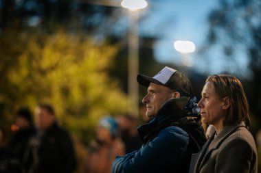 İnsanlar Kino Pedalis festivali sırasında ön planda tanıtım pankartıyla merdivenlerde oturup açık hava film gösterimi izliyor. 10.05.2025 Valmiera, Letonya