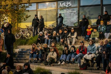 İnsanlar Kino Pedalis festivali sırasında ön planda tanıtım pankartıyla merdivenlerde oturup açık hava film gösterimi izliyor. 10.05.2025 Valmiera, Letonya