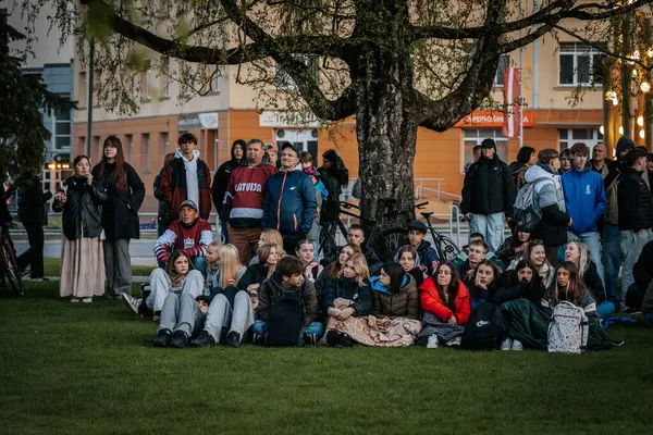 Bir grup insan büyük bir LED ekranda spor maçı izlemek için dışarıda toplandı. Kırmızı elbiseli taraftarlar tezahürat yapıyordu. Hokey hayranları canlı yayın izliyor. 10.05.2025 Valmiera, Letonya