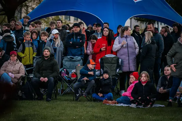 Bir grup insan büyük bir LED ekranda spor maçı izlemek için dışarıda toplandı. Kırmızı elbiseli taraftarlar tezahürat yapıyordu. Hokey hayranları canlı yayın izliyor. 10.05.2025 Valmiera, Letonya