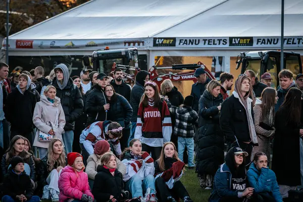 Çoğu battaniye ve sırt çantalarıyla çimlerin üzerinde oturan bir grup insan, serin havada bir açık hava etkinliğini dikkatle izliyor. 10.05.2025 Valmiera, Letonya