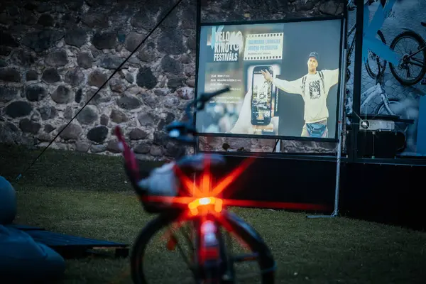 Sıcak ceketli ve şapkalı insanlar, Kino Pedlis festivali sırasında açık ekrana yansıtılan ve rahat armut çuvalları ve bayrak ile çevrili bir film izliyorlar. 10.05.2025 Valmiera, Letonya