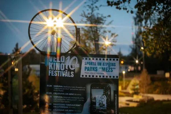 Letonya 'nın Valmiera kentindeki Velo Kino Festivalleri için bir arka ışıklandırma tabelası. Bisiklet tekeri ve parlak sokak lambaları alacakaranlıkta yıldız patlaması etkisi yaratıyor. 10.05.2025 Valmiera, Letonya