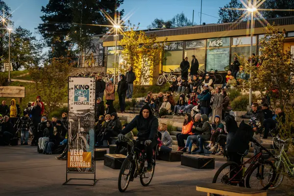 İnsanlar Kino Pedalis festivali sırasında ön planda tanıtım pankartıyla merdivenlerde oturup açık hava film gösterimi izliyor. 10.05.2025 Valmiera, Letonya