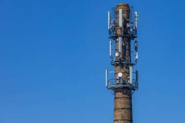 Birden fazla modern hücresel anten ve uydu antenleri ile donatılmış, parlak mavi gökyüzüne karşı yeniden tasarlanmış bir tuğla bacası. Cömert kopya alanı içerir.