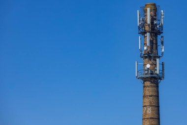 Birden fazla modern hücresel anten ve uydu antenleri ile donatılmış, parlak mavi gökyüzüne karşı yeniden tasarlanmış bir tuğla bacası. Cömert kopya alanı içerir.