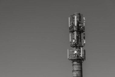 Birden fazla modern hücresel anten ve uydu antenleri ile donatılmış, parlak mavi gökyüzüne karşı yeniden tasarlanmış bir tuğla bacası. Cömert kopya alanı içerir.