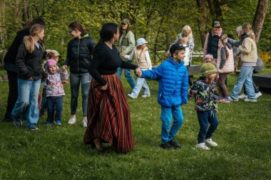 Aileler ve çocuklar renkli kiraz çiçekleriyle dekore edilmiş tuğla bir avluda yürürler, şenlikli, topluma odaklı bir atmosfer yaratırlar. 17.05.2025 Valmiera, Letonya