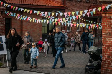 Aileler ve çocuklar renkli kiraz çiçekleriyle dekore edilmiş tuğla bir avluda yürürler, şenlikli, topluma odaklı bir atmosfer yaratırlar. 17.05.2025 Valmiera, Letonya