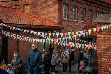 Aileler ve çocuklar renkli kiraz çiçekleriyle dekore edilmiş tuğla bir avluda yürürler, şenlikli, topluma odaklı bir atmosfer yaratırlar. 17.05.2025 Valmiera, Letonya