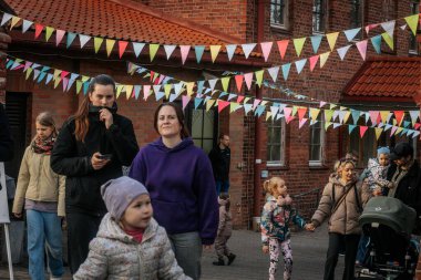 Aileler ve çocuklar renkli kiraz çiçekleriyle dekore edilmiş tuğla bir avluda yürürler, şenlikli, topluma odaklı bir atmosfer yaratırlar. 17.05.2025 Valmiera, Letonya