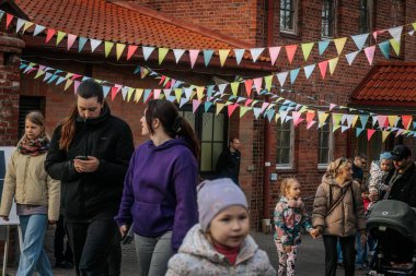 Aileler ve çocuklar renkli kiraz çiçekleriyle dekore edilmiş tuğla bir avluda yürürler, şenlikli, topluma odaklı bir atmosfer yaratırlar. 17.05.2025 Valmiera, Letonya