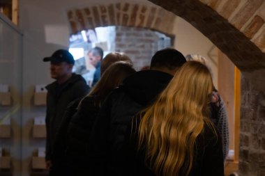 Bir grup insan müze gibi bir yerde toplanıyor ve duvarlarda ve tavanda geleneksel ahşap aletler sergileniyor. Işıklandırma sıcak ve bastırılmış. 17.05.2025 Valmiera, Letonya