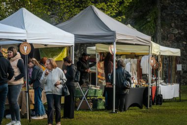 İnsanlar, el yapımı eşyalar, yerel yiyecekler ve el sanatları sunan bir açık hava pazarındaki teçhizat çadırlarının altındaki 17.05.2025 Valmiera, Letonya