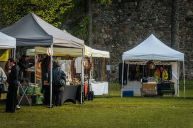 İnsanlar, el yapımı eşyalar, yerel yiyecekler ve el sanatları sunan bir açık hava pazarındaki teçhizat çadırlarının altındaki 17.05.2025 Valmiera, Letonya