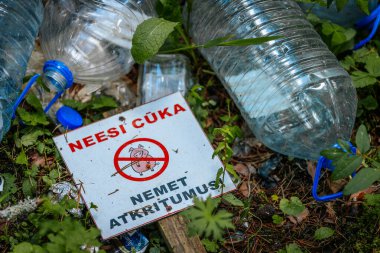 Letonya 'da çöp atmamak için uyarıda bulunan bir işaret, ormanda plastik şişeler ve çöplerle çevrili yerde yatıyor. 18.05.2025 Valmiera, Letonya