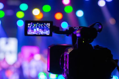 Profesyonel video kamera canlı bir konser ya da etkinlik kaydediyor, sahneyi gösteren bir ekran ve arka planda parlak renkli ışıklar. 22.05.2025 Valmiera, Letonya