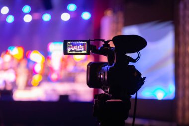 Profesyonel video kamera canlı bir konser ya da etkinlik kaydediyor, sahneyi gösteren bir ekran ve arka planda parlak renkli ışıklar. 22.05.2025 Valmiera, Letonya